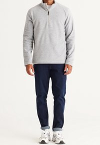 Grå fleecepullover med kvart-lynlås krave, kombineret med mørkeblå jeans og hvide sportssko, med op rullede ærmekanter.