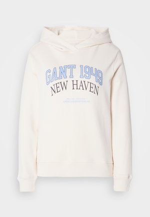 Kreminės spalvos džemperis su užrašu "GANT 1949" šviesiai mėlyna spalva, "NEW HAVEN" juoda spalva, ir mažesniu šviesiai mėlynu tekstu žemiau, be matomų kišenių.