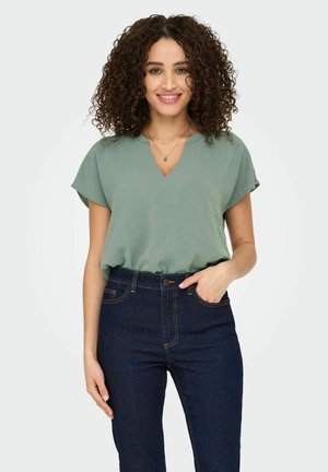 Grøn kortærmet V-hals top kombineret med mørk denim højtaljede jeans. Toppen har en afslappet pasform og blød tekstur.