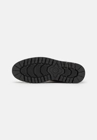 Suela de zapato de goma negra con una superficie texturada, que presenta un patrón de banda de rodadura multidireccional y un diseño elevado central para mejorar el agarre.