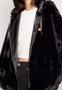 Zwarte nepbonten hoodie met een rits aan de voorkant en satijnen voering. Bevat een opvallende binnenzak met een oranje accent. Cropped ontwerp.