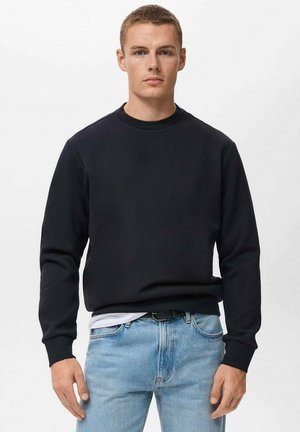 Black crewneck sweatshirt in a soft fabric, featuring ribbed cuffs and hem, paired with light blue jeans. Simple, classic design.