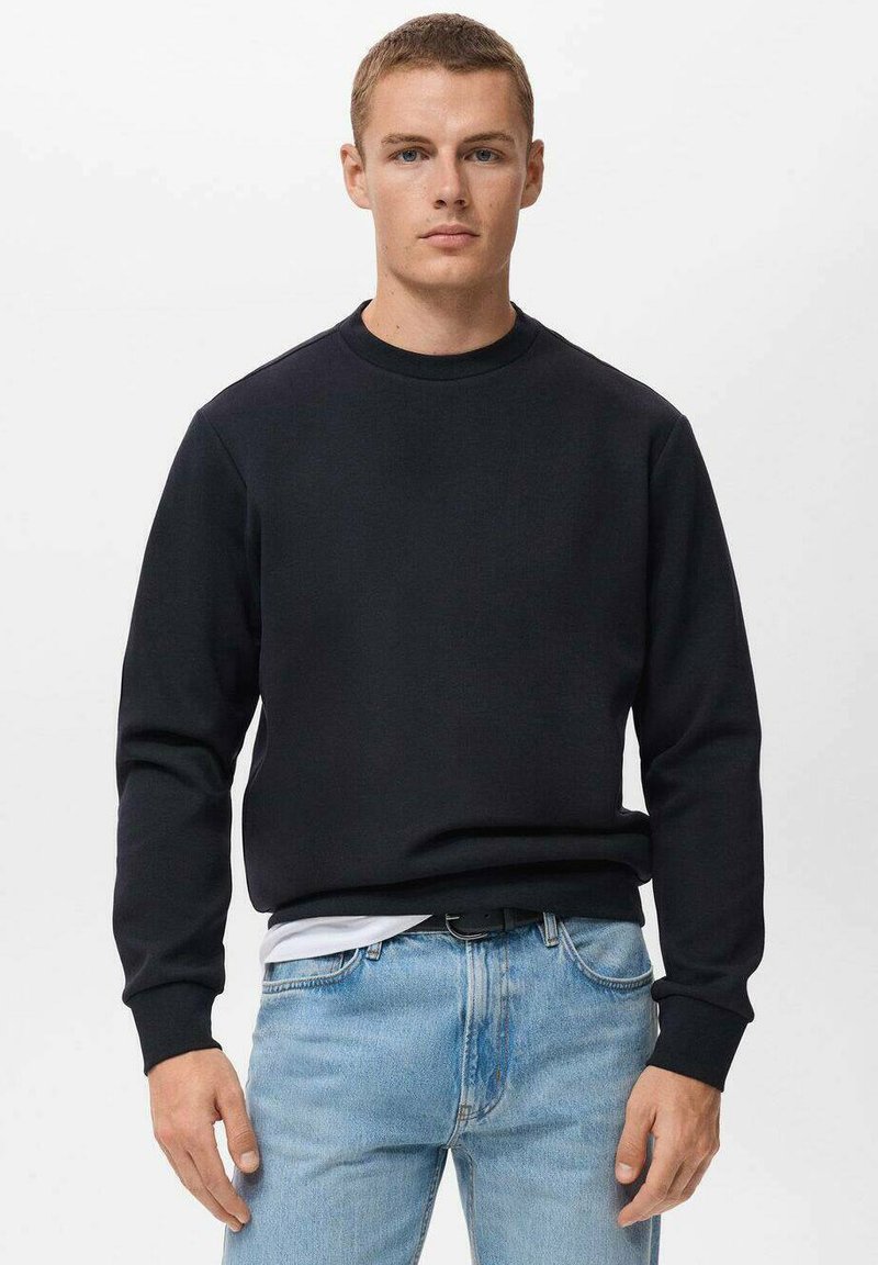 Zwarte crewneck sweatshirt in een zachte stof, met ribbels aan de mouwen en onderkant, gecombineerd met lichtblauwe jeans. Eenvoudig, klassiek ontwerp.