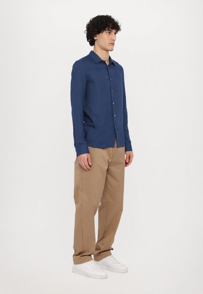 Marineblauwe overhemd met lange mouwen en knoopsluiting, gemaakt van lichte stof. Gecombineerd met beige broek en witte sneakers.