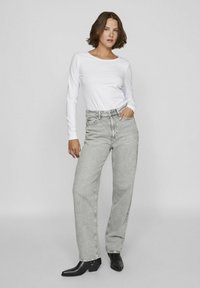 Vit långärmad skjorta i kombination med grå högmidjade vida jeans och svarta ankelboots. Enkelt design, texturerade tyger, rena linjer.