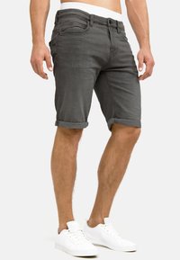 Shorts de mezclilla gris con dobladillos enrollados, bolsillos frontales y cremallera. Combinados con zapatillas blancas para un look casual.