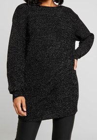 Musta neulottu neulepaita väljällä siluettilla, jossa on metallinhohtoisia lankoja kimallusta varten, pitkät hihat ja pyöreä kaula-aukko.