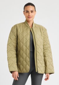 Olijfgroene gewatteerde jas met een ruitpatroon, geribde kraag en een rits aan de voorkant. Beschikt over ontspannen, brede mouwen en minimale branding.