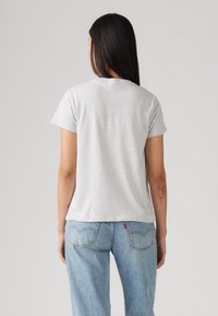 Grå bomullströja med rund hals och korta �ärmar, med en avslappnad passform. Den är ihop med ljusblå denimjeans.