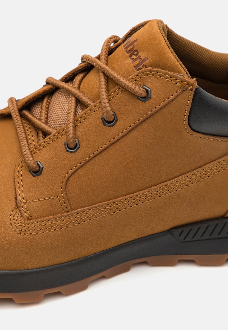 Bruine leren wandelschoen met een gestructureerd oppervlak, ronde veters en een zwarte rubberen zool met een profiel voor grip.