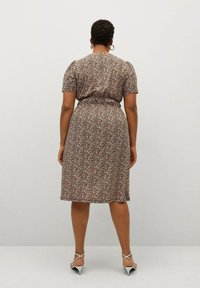 Vestido floral con mangas cortas, fondo marrón, pequeñas flores multicolores, cintura ajustada, hasta la rodilla, combinado con tacones blancos con tiras.