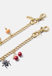Collana in tonalità oro con chiusure a gancio, caratterizzata da tre ciondoli: ragno nero, ciliegie rosse e fungo arancione. Maglie testurizzate e rifiniture lucide.