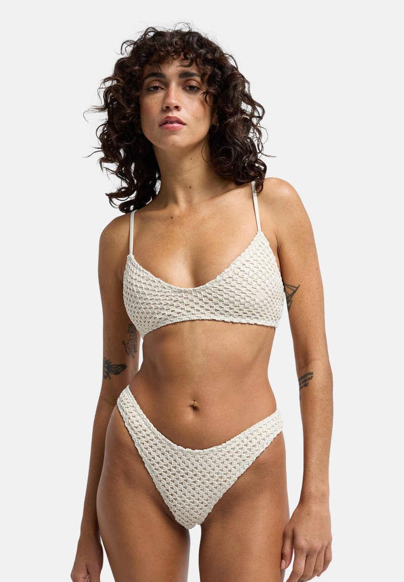 Ensemble bikini en crochet de couleur crème. Le haut présente une forme triangulaire avec des bretelles fines, tandis que le bas est taille haute avec une coupe échancrée.