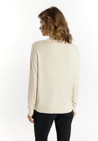 Cream knit sweater with long sleeves, a ribbed neckline, and a relaxed fit. Smooth texture and hemline. Paired with black pants.