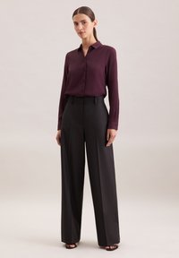 Bordeauxrotes Langarm-Hemd mit Knopfleiste, kombiniert mit hochgeschnittenen schwarzen weiten Hosen. Glattes Material mit klassischem Kragen und taillierter Passform.