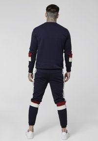 Sudadera azul marino y joggers a juego, hechos de tela suave. Presentan acentos en rojo y blanco en las mangas y los lados de los pantalones, con detalles del logo.