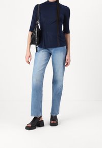 Navy blue short-sleeve top with a high neckline, light blue straight-leg jeans, and black chunky heeled sandals. Black shoulder bag included.