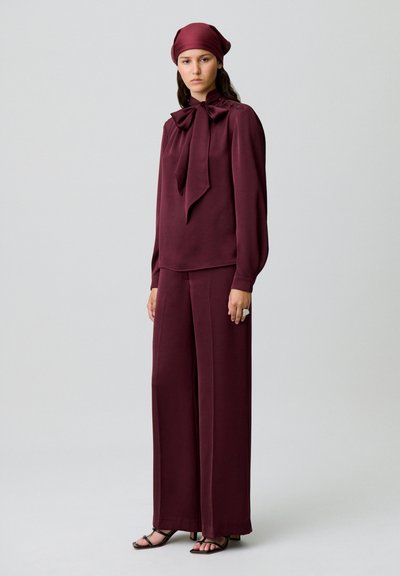 Completo bordeaux in due pezzi composto da una blusa con fiocco e pantaloni a gamba larga, realizzato in tessuto liscio con una texture soffice.