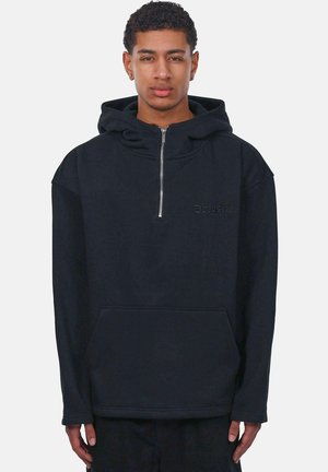 Schwarze Zip-Hoodie mit Kängurutasche, aus weichem Material gefertigt. Verfügt über eine verstellbare Kapuze und ein dezentes, geprägtes Logo auf der Brust.