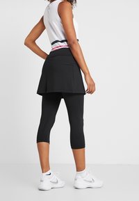Falda-pantalón negra de tenis sobre leggings capri negros, combinada con una camiseta sin mangas blanca con rayas horizontales rosas y verdes en la cintura.