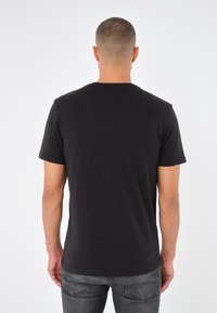 Czarny bawełniany t-shirt z krótkimi rękawami i okrągłym dekoltem, o gładkiej fakturze i prostym kroju, noszony z szarymi jeansami.