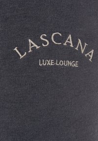 Koolgrijze stof met een zachte textuur, voorzien van geborduurde tekst: "LASCANA LUXE-LOUNGE" in lichtbeige, gecentreerd ontwerp.