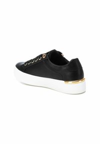 Zapatilla negra de caña baja con suela de plataforma blanca, ojales dorados para los cordones y un acento dorado en el talón, en un ángulo que muestra el lateral externo y la parte trasera.