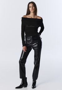 Czarny top na ramiączkach z teksturowanej tkaniny i srebrnym napisem; w połączeniu z czarnymi spodniami z sztucznej skóry w wysokim stanie; gładkie botki za kostkę.