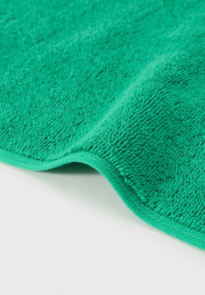 Φωτεινό πράσινο πανί μικροϊνών με ορατή υφή και ραμμένα άκρα, που βρίσκεται μερικώς διπλωμένο σε μια λευκή επιφάνεια.