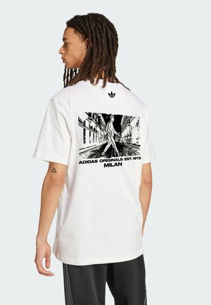 Weißes Baumwoll-T-Shirt mit einem schwarzen Grafikdruck auf der Rückseite, der eine Straßenszene mit einer Person, die geht, zeigt. Adidas-Logo im oberen Rückenbereich.