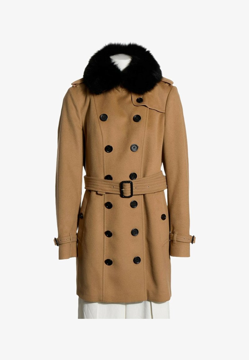 Manteau croisé couleur camel avec boutons noirs, col en fourrure noire, taille cintrée par une ceinture et détails de sangles sur les manches.