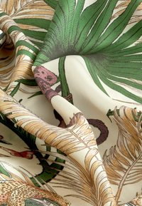 Tela estampada con hojas de palma verdes y acentos marrones sobre un fondo crema, destacando ilustraciones detalladas y una textura suave.