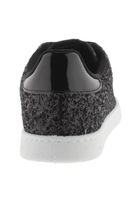 Svart glittrande sneaker med glänsande svart hälflik och vit gummisula, sedd bakifrån.