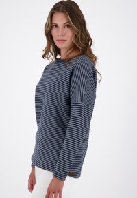 Maglietta a maniche lunghe blu navy con strisce orizzontali bianche, dotata di un colletto rotondo e di una piccola etichetta in tessuto sul lato sinistro.