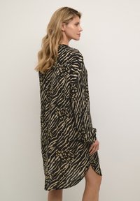 Abito a maniche lunghe con stampa animale nera e oro, caratterizzato da una vestibilità comoda e spacchi laterali per facilità di movimento.