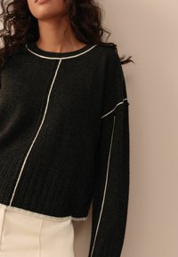 Maglione nero con cuciture bianche a contrasto, caratterizzato da un orlo a costine e maniche ampie. Texture morbida e design cropped per un look contemporaneo.