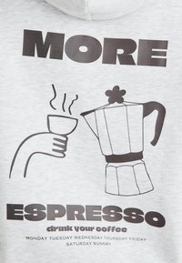 Grå huvtröja med svart grafisk design som föreställer en kaffekoppen, en kaffekanna och texten: "MER ESPRESSO drick ditt kaffe" i fet stil.