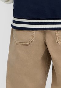 Marine bomberjack met witte gestreepte ribbels aan de manchetten, in combinatie met beige broek met schuine achterzakken en een gladde, matte textuur.