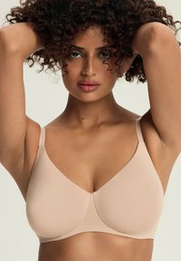 Beżowy bezszwowy biustonosz z regulowanymi ramiączkami, gładkim wykończeniem i trójkątnym kształtem miseczek, odpowiedni dla komfortu i wsparcia.