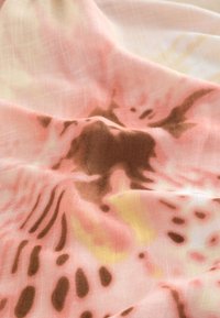 Soft fabric with a blurred abstract pattern in pink, brown, and yellow tones, showing gentle folds and texture.