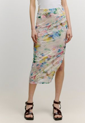 Bloemen midi-rok van een pastelstof met meerkleurige bloemen, asymmetrische zoom en een gedrapeerd ontwerp. Gecombineerd met hoge sandalen.