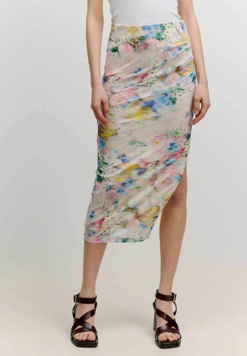 Bloemen midi-rok van een pastelstof met meerkleurige bloemen, asymmetrische zoom en een gedrapeerd ontwerp. Gecombineerd met hoge sandalen.