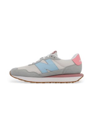 Zapatilla blanca y gris con logo azul "N", lengüeta rosa en el talón, cordones blancos y suela de goma, mostrada de perfil sobre fondo blanco.