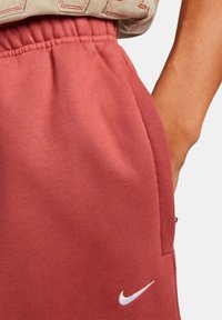 Pantalones cortos de algodón rojos con una cintura elástica y bolsillos laterales. Un sutil logo de Nike se muestra en blanco en la parte inferior derecha.
