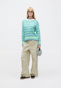 Light blue knitted sweater with a patterned design, paired with loose plaid beige trousers and black platform shoes. Holding a gray bag.