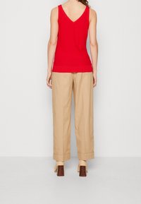 Červený bezrukávový pletený top s V-výstřihem, doplněný o volné béžové kalhoty. Kalhoty mají manžetové zakončení a jemnou texturu.