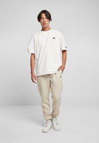 Witte T-shirt met korte mouwen en een klein zwart logo, gecombineerd met lichtbeige joggingsbroek en witte sneakers. Zachte katoenstof met een relaxte pasvorm.