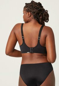 Sujetador negro con tirantes ajustables y un cierre de gancho en la parte trasera. Tela suave con un diseño simple, acompañado de ropa interior negra.