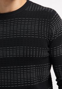 Maglione nero a maglia caratterizzato da un motivo testurizzato con sfumature di grigio, scollatura rotonda e design aderente.