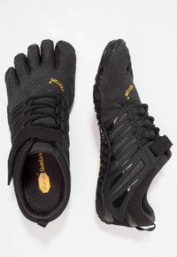 Czarne minimalistyczne buty z projektem pięciu palców, teksturowaną cholewką, elastyczną podeszwą i regulowanym paskiem, wykonane z lekkiego materiału.